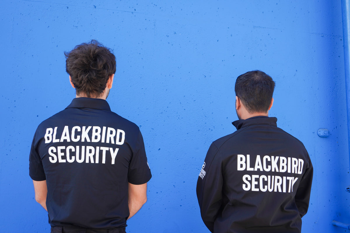 Two security personnel wearing Blackbird Security uniforms against a blue wall.