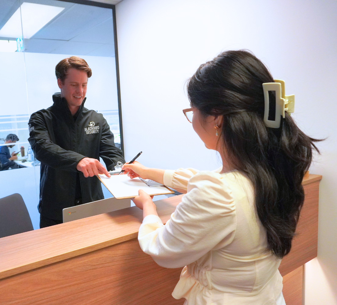 Security officer is asking a visitor to sign the document on a clipboard at the desk of a corporate office building.