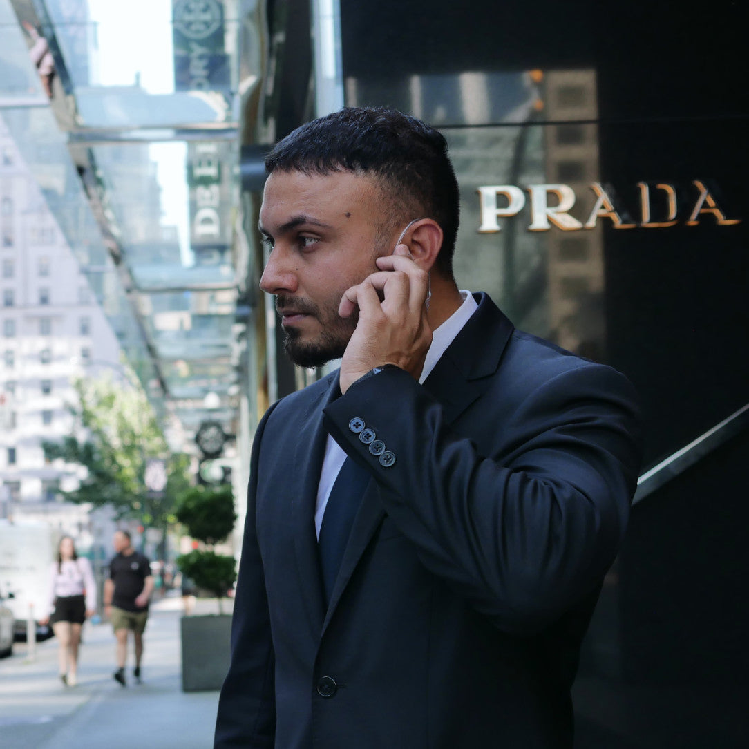 A suit and tie security guard touching earpiece communication device outside of a Prada store