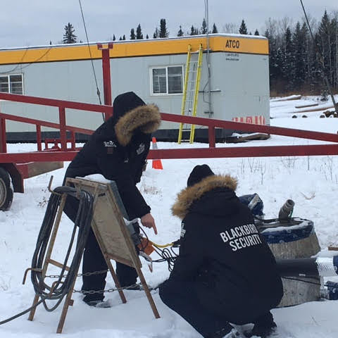 a pair of security guards in winter jackets inspecting equipment at a remote job site