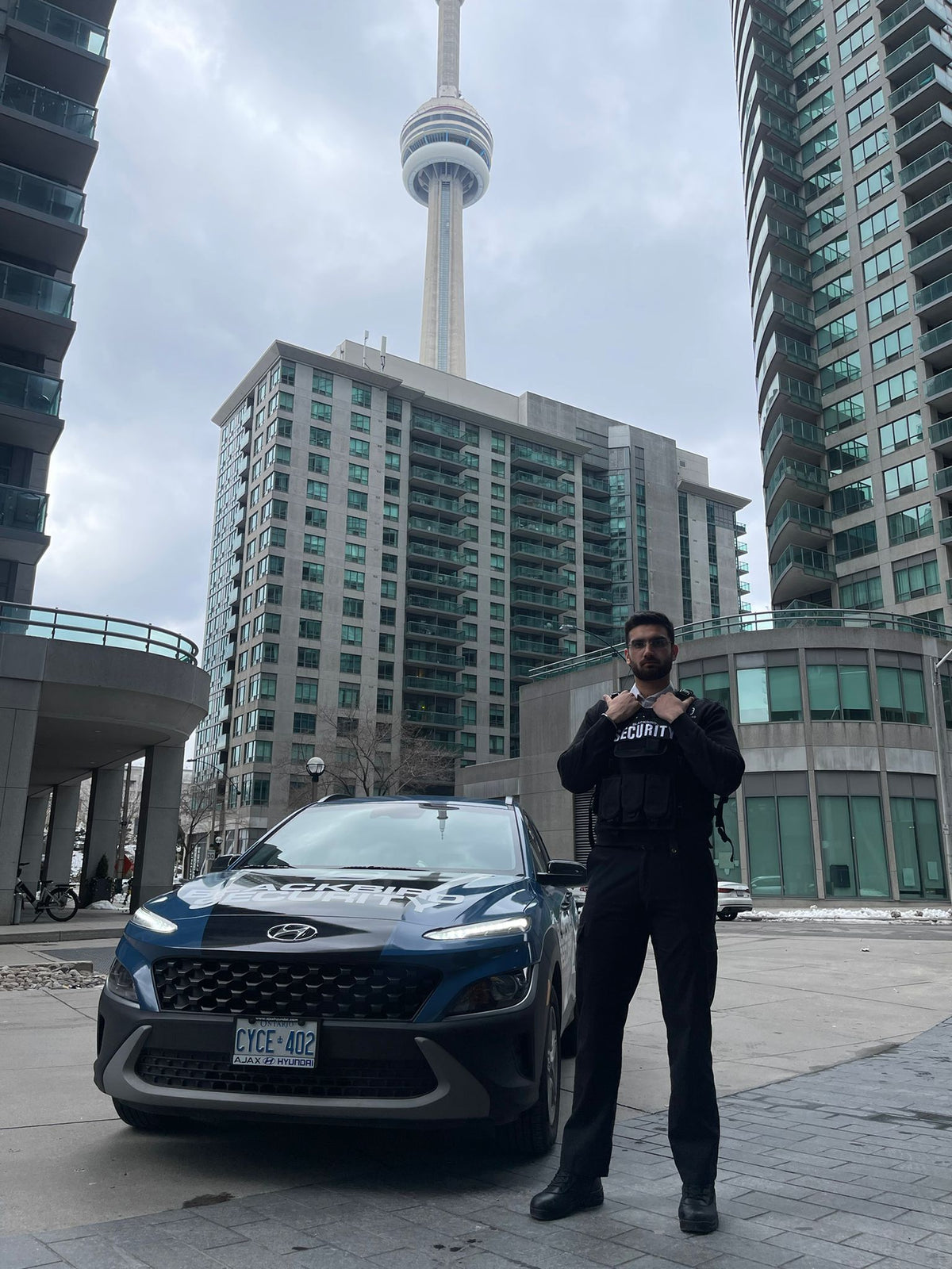 Uniformed Blackbird security guard in front of Mobile patrol car with CN tower in background