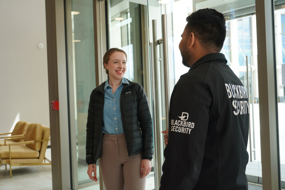 Man wearing a Blackbird Security jacket holding a condo lobby door open for a woman.