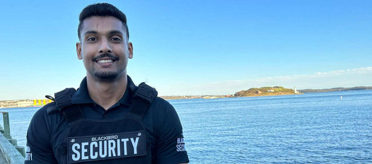 Man wearing a security vest with 'Blackbird Security' on a waterfront background