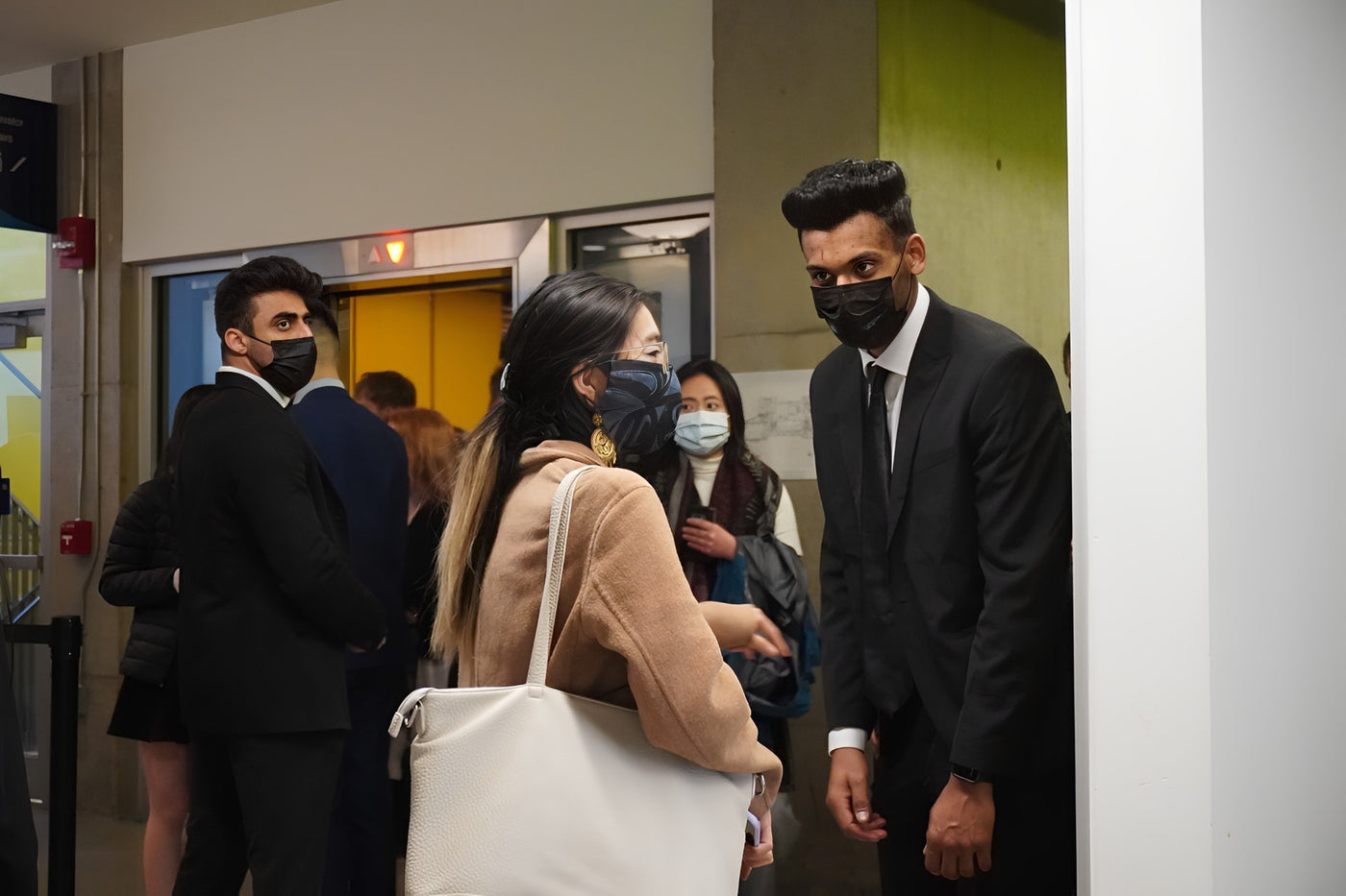 A woman with a large bag goes through a security check by a uniformed security guard dressed in a suit and tie