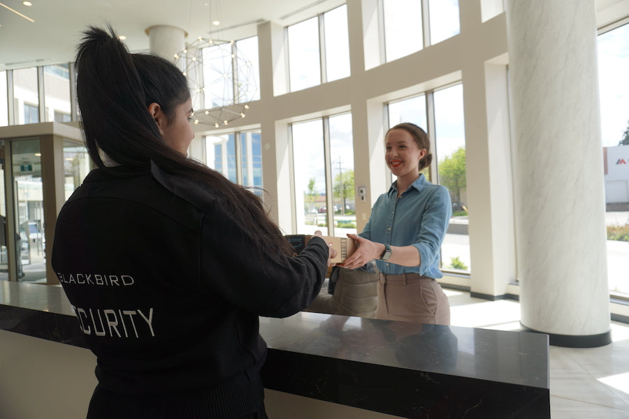 A concierge security guard hands a resident a package from behind a desk.