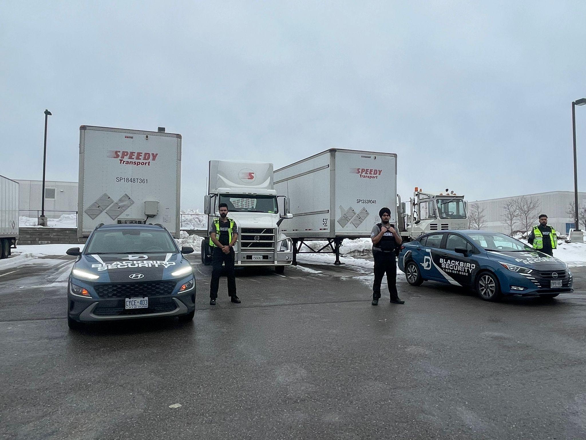 Three Uniformed Blackbird security guards in front of Mobile patrol car and transport trucks