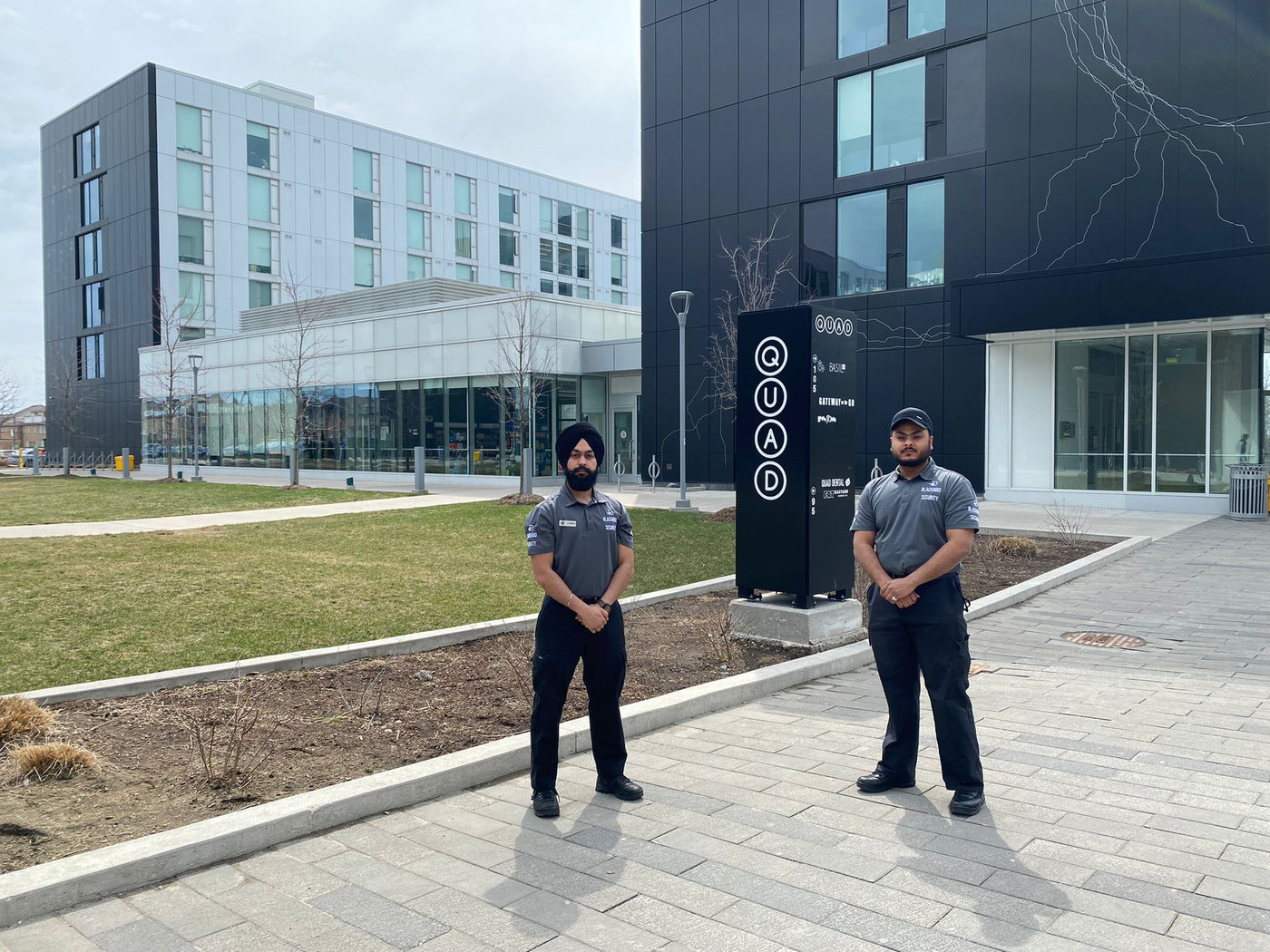 Two uniformed security guards stand outside an educational building to provide foot patrols and campus security