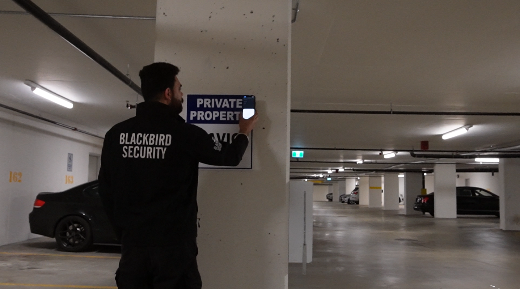 Uniformed Blackbird security guard patrolling parkade and checking security tag