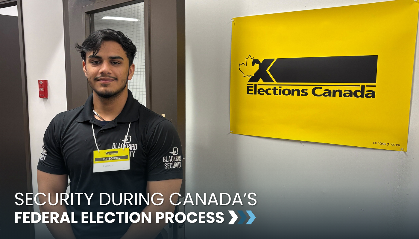 A Blackbird Security election security guard during the Canadian Federal Election. The guard is smiling at the camera, wearing a black t-shirt embroidered with the Blackbird Security logo, and is standing next to an Elections Canada poster.