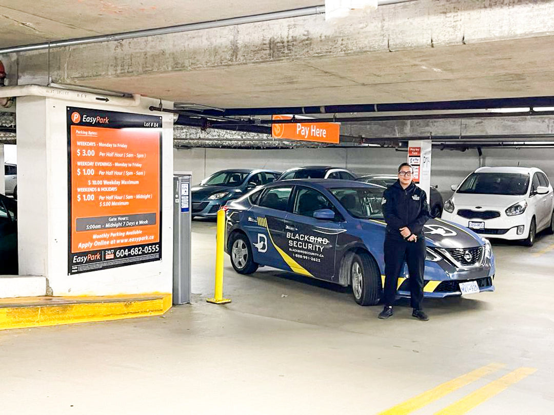 Uniformed blackbird security guard in front of mobile patrol car in underground parking