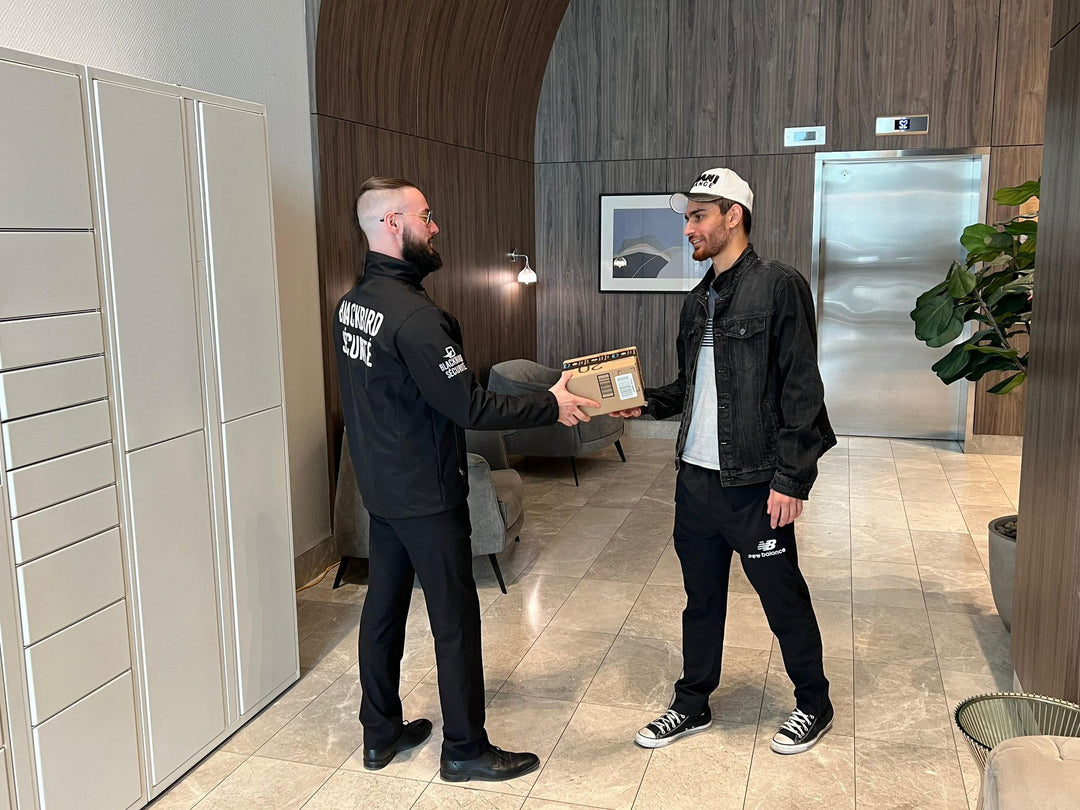 Uniformed Blackbird security guard handing condo resident a package