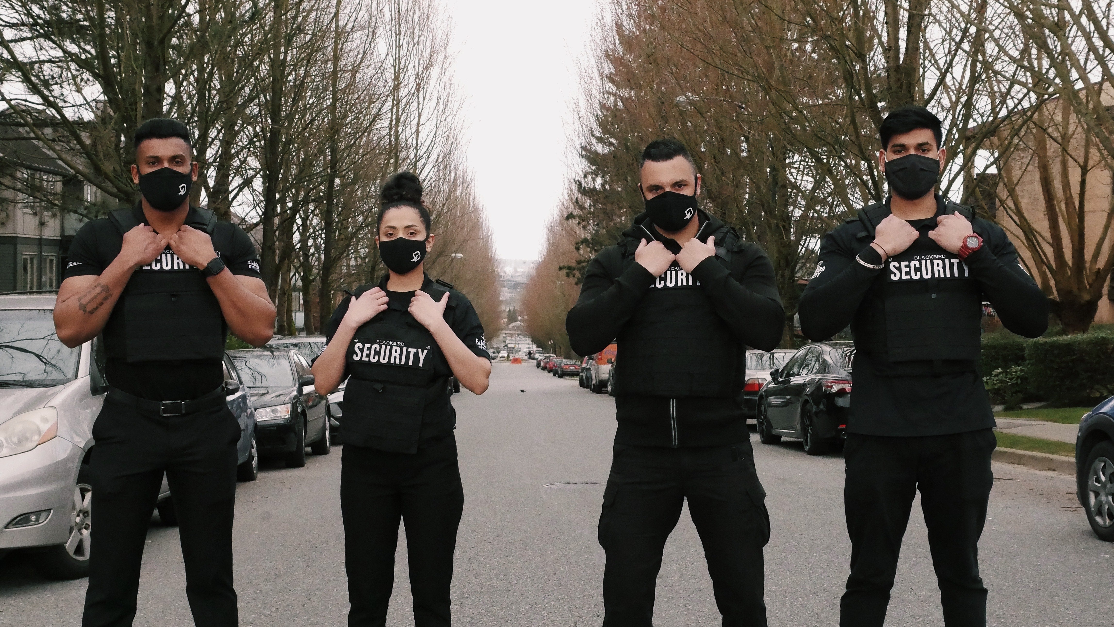 Four masked Uniformed Blackbird security guards standing on street