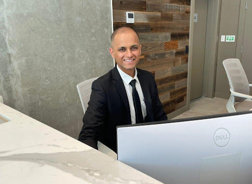 A security guard in a suit and tie sits behind a concierge desk smiling