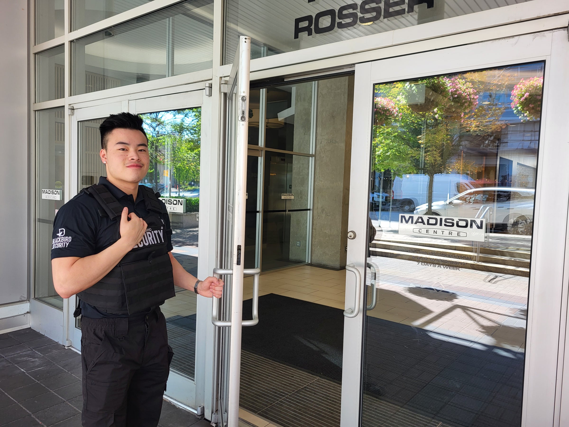 Uniformed Blackbird security guard standing in front of building holding door open