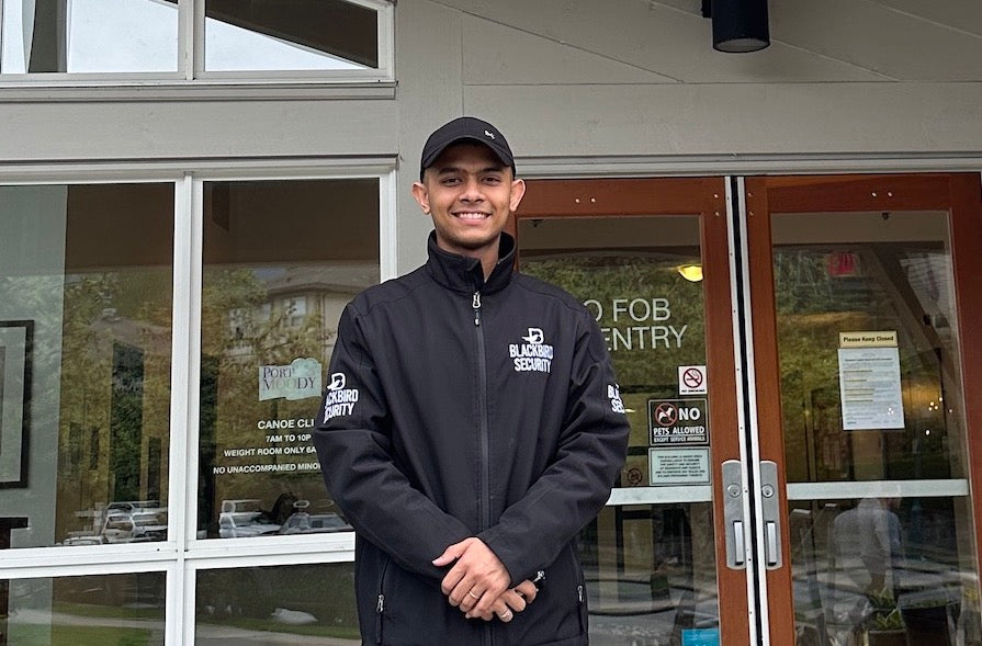 A smiling Blackbird security guard stands outside of the doors of a building with Canoe Club signage