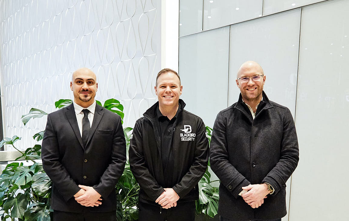 Three uniformed Blackbird Security professionals smiling against a white background and plants