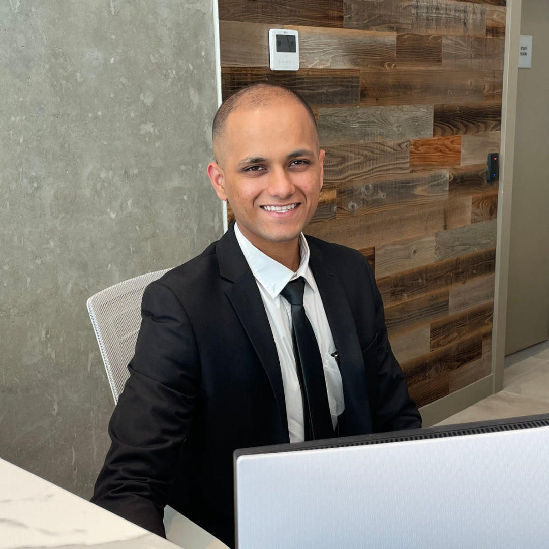 A smiling man in a black suit setting at a desk