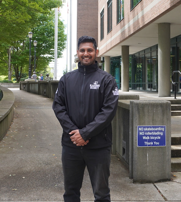 Blackbird Security officer stands in front of a government building. Their hands are in front of them in a relaxed pose, and they are smiling.