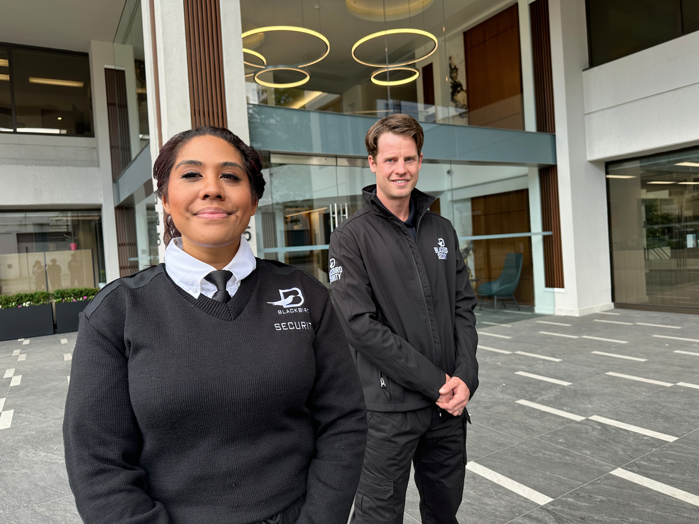 A pair of smiling Blackbird security guards stand outside of a commercial building