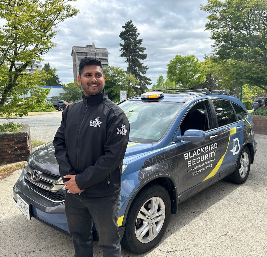 Uniformed Blackbird Security guard is standing in front of mobile security patrol vehicle on a cloudy day