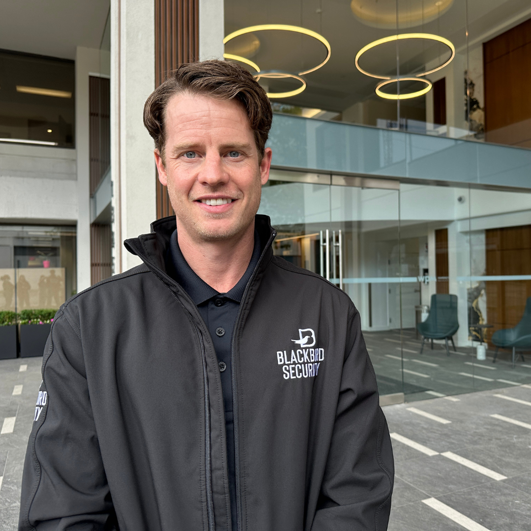 A smiling Blackbird security guard stands outside of a commercial building