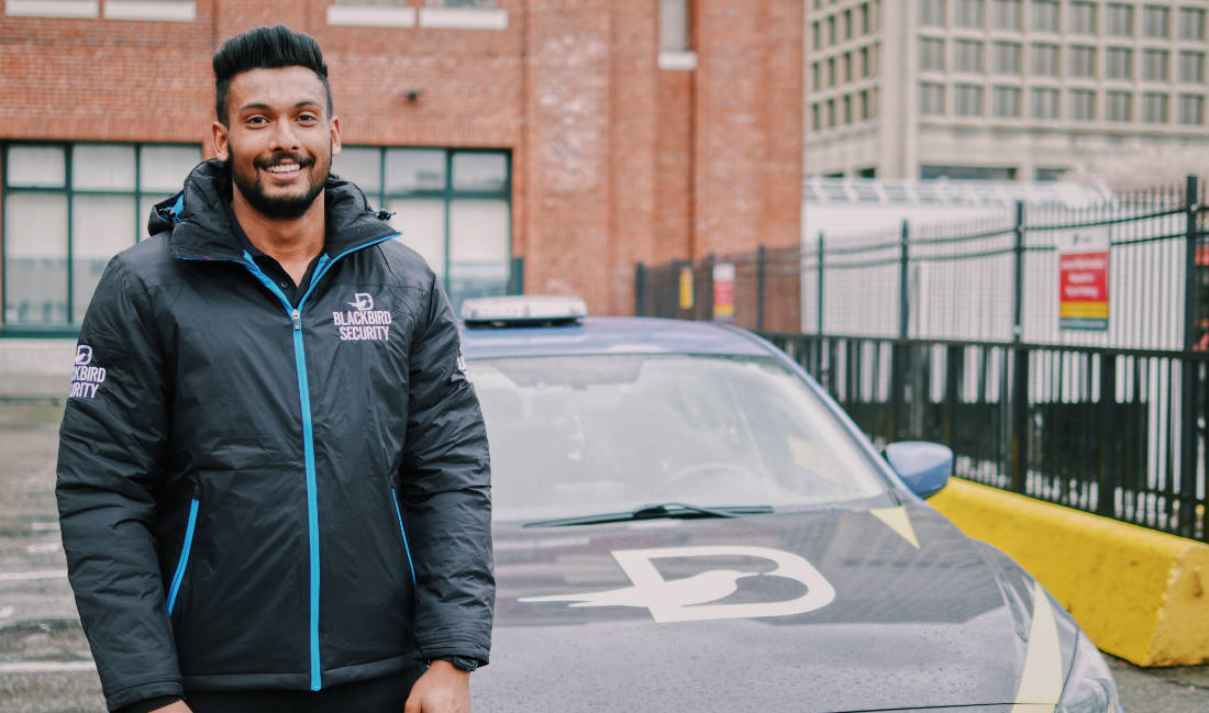 Uniformed Security guard standing in front of mobile patrol vehicle and smiling