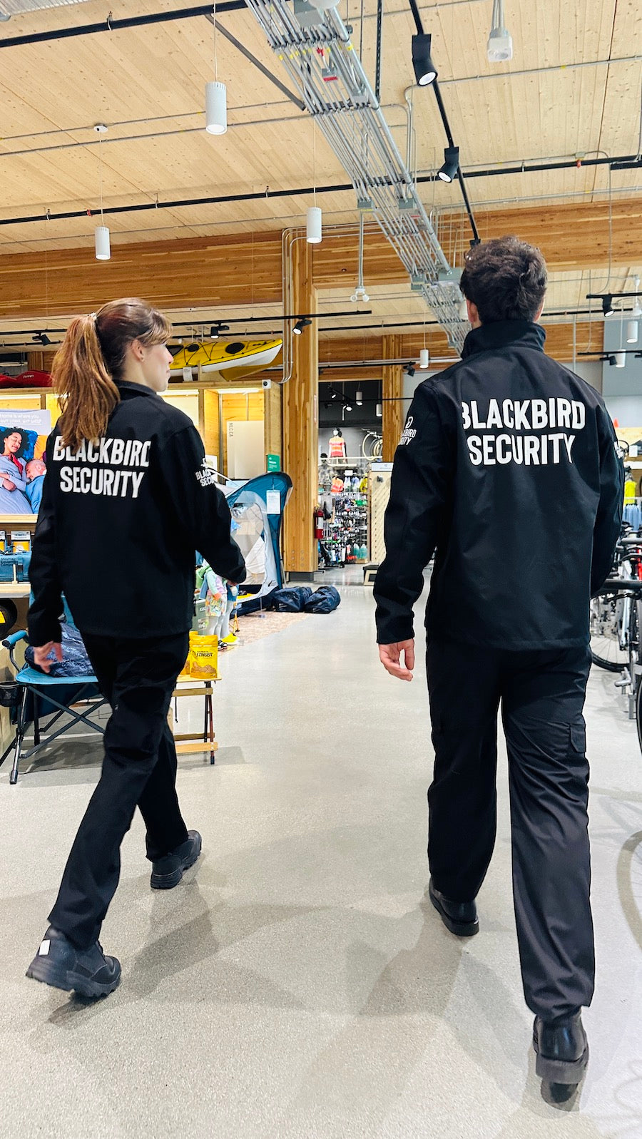 Two security officers are walking away from the camera inside a retail store in Regina. The back of their jackets read Blackbird Security.