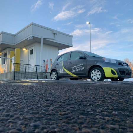 Mobile patrol security car parked outside an industrial site gatehouse